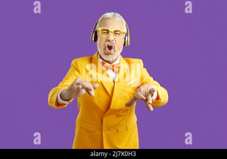 Allegro uomo alto grigio-capelli posa isolato su sfondo viola parete ritratto studio. Concetto di stile di vita delle persone. Ascolta la musica con le cuffie Foto Stock
