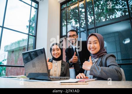 il team aziendale si mostra con il pollice mentre si siede in ufficio Foto Stock