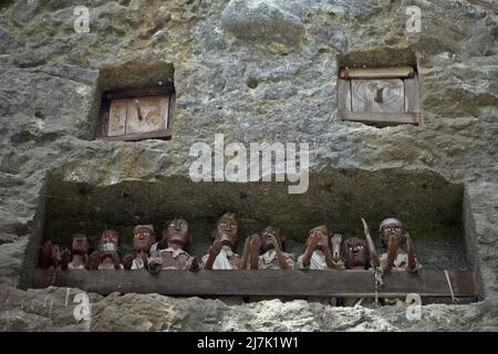 Aperture di tombe in pietra e effigi in legno su una scogliera in un tradizionale luogo di sepoltura a Lemo, Nord Toraja, Sud Sulawesi, Indonesia. Foto Stock