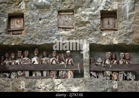 Aperture di tombe in pietra e effigi in legno su una scogliera in un tradizionale luogo di sepoltura a Lemo, Nord Toraja, Sud Sulawesi, Indonesia. Foto Stock