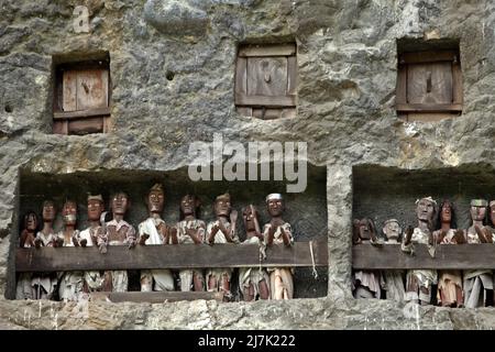 Aperture di tombe in pietra e effigi in legno su una scogliera in un tradizionale luogo di sepoltura a Lemo, Nord Toraja, Sud Sulawesi, Indonesia. Foto Stock