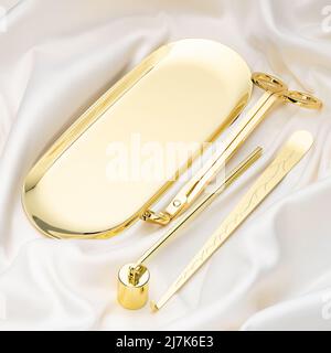 Un set di quattro accessori color oro per l'uso di candele aromatiche. Un estintore a candela, un vassoio portaoggetti, un cucchiaia per stoppino e un rifinitore su un tessuto di seta Foto Stock