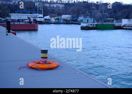Anello di Lifebuoy sul ormeggio vicino al bullard con vista mare di Marina Mariupol, Ucraina all'aperto Foto Stock