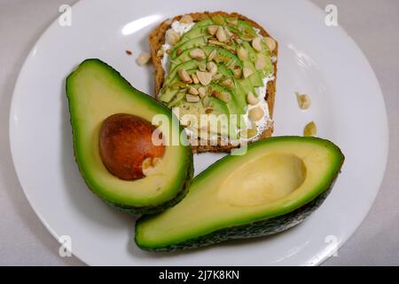 Panini all'avocado, metà dell'avocado, con arachidi e semi di zucca su sfondo bianco e frutta di avocado divisa Foto Stock