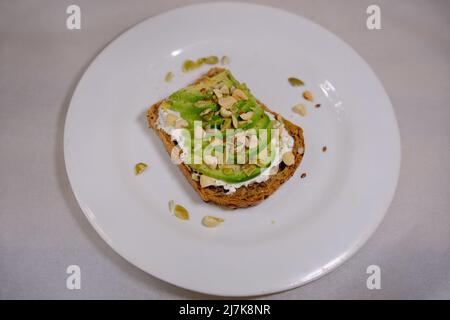Panini all'avocado, metà dell'avocado, con arachidi e semi di zucca su sfondo bianco Foto Stock