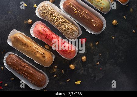 Dessert tradizionale francese. Eclairs assortiti su sfondo di pietra scuro. piatto, banner Foto Stock