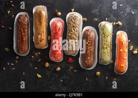 Dessert tradizionale francese. Eclairs assortiti su sfondo di pietra scuro. piatto, banner Foto Stock