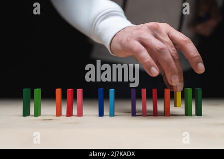 Foto concettuale di una mano che mette una pietra ad una fila di pietre domino. Effetto domino con pietre colorate e copyspace Foto Stock