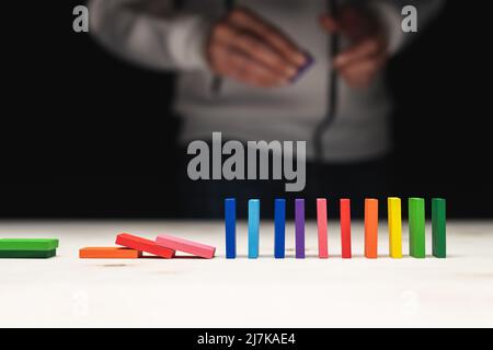 Foto concettuale di una mano che mette una pietra ad una fila di pietre domino. Effetto domino con pietre colorate e copyspace Foto Stock