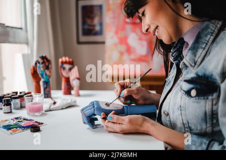 Giovane artista che dipinge legno opere d'arte a mano all'interno dello studio d'arte interni - Focus on hand holding brush Foto Stock