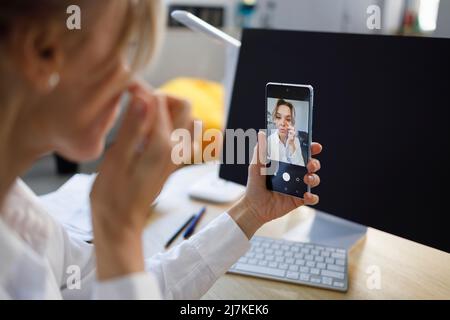 Donna d'affari che corregge il trucco guardando la fotocamera dello smartphone Foto Stock