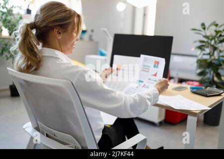 Una donna d'affari di mezza età guarda rapporto finanziario che analizza il reddito Foto Stock