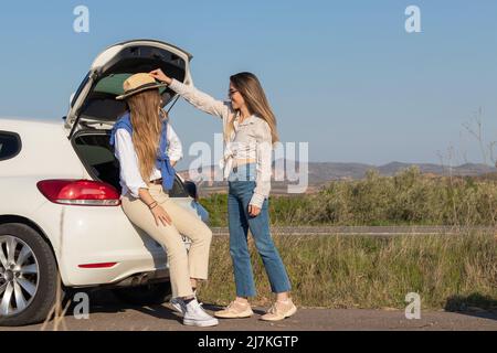 Buone amiche che giocano in giro e si divertono nel bel mezzo del nulla in una sosta del loro viaggio di rottura frettolosi Foto Stock