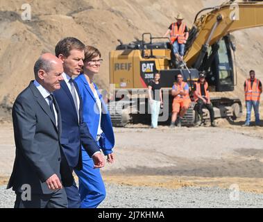 10 maggio 2022, Brandeburgo, Cottbus: OLAF Scholz (l-r, SPD), Cancelliere tedesco, Richard Lutz, Amministratore Delegato del DB, E Daniela Gerd, membro del consiglio di amministrazione del DB per la digitalizzazione e la tecnologia, si dirigono attraverso il cantiere per la cerimonia simbolica e innovativa di un nuovo impianto ferroviario. Deutsche Bahn ha iniziato la costruzione del nuovo stabilimento ferroviario di Cottbus. Il primo di quelli che saranno due workshop è in fase di costruzione qui. I primi treni ICE 4 saranno mantenuti in questa sala in soli due anni. Nel cantiere, palloncini rossi simboleggiavano i primi 500 nuovi posti di lavoro e apprendistato che verranno creati qui da Foto Stock