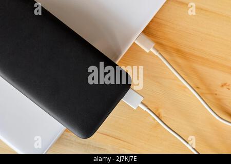 Power Bank carica un computer portatile tramite cavo USB di tipo C su sfondo in legno Foto Stock