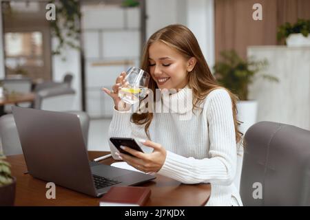 Bella donna seduta al tavolo in ufficio e bere acqua Foto Stock