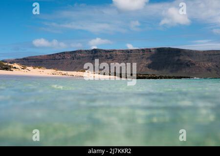 Basso angolo di acque marine limpide lavando scogliera rocciosa sulla costa sotto il cielo blu con le nuvole Foto Stock