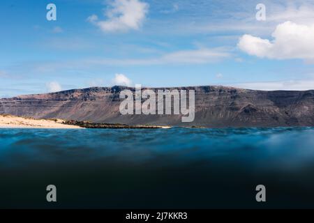 Basso angolo di acque marine limpide lavando scogliera rocciosa sulla costa sotto il cielo blu con le nuvole Foto Stock
