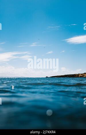 Basso angolo di acque marine limpide lavando scogliera rocciosa sulla costa sotto il cielo blu con le nuvole Foto Stock