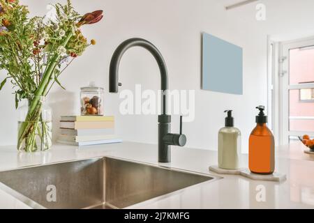 Lavandino con rubinetto nero e dispenser di sapone posti sul banco con bouquet di fiori freschi in vaso in cucina moderna Foto Stock