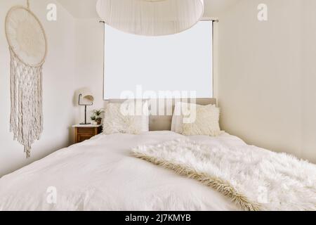 Comodo letto con coperta in pelliccia e cuscini posizionati in luce spazioso con macrame Dream catcher Foto Stock