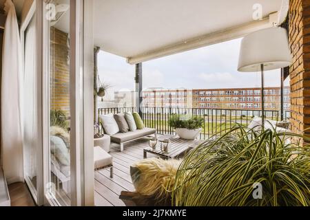 Comodi divani con cuscini e poltrone posti vicino a un tavolo in legno sulla terrazza con porta d'ingresso in vetro del moderno edificio residenziale Foto Stock