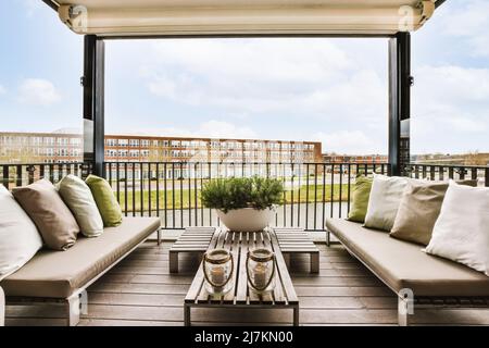 Comodi divani con cuscini e poltrone posti vicino a un tavolo in legno sulla terrazza con porta d'ingresso in vetro del moderno edificio residenziale Foto Stock