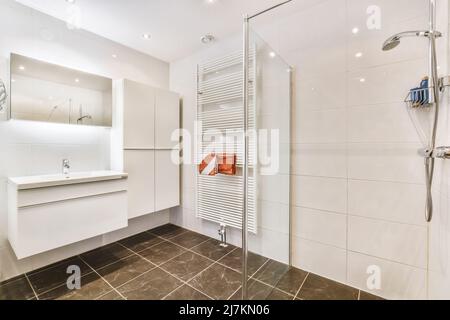 Lavandino bianco a parete con specchio collocato in un elegante e spazioso bagno con cabina doccia in vetro e scaldasalviette radiatore Foto Stock