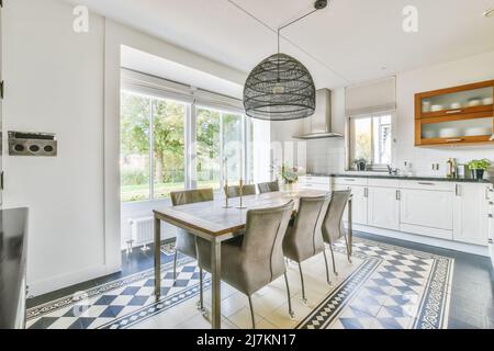 Comode sedie al tavolo da pranzo decorate con fiori e candele poste in stile classico spaziosa cucina con armadi bianchi nella villa Foto Stock