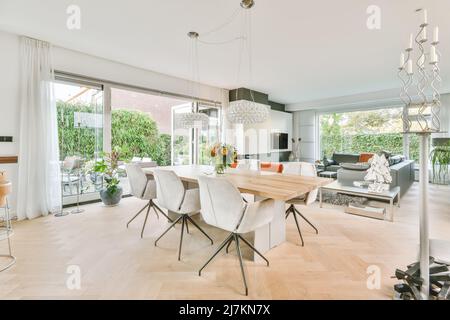 Comodo divano e poltrone appoggiati contro la TV moderna e camino in un elegante e luminoso soggiorno con porte di vetro vicino al tavolo da pranzo a casa Foto Stock