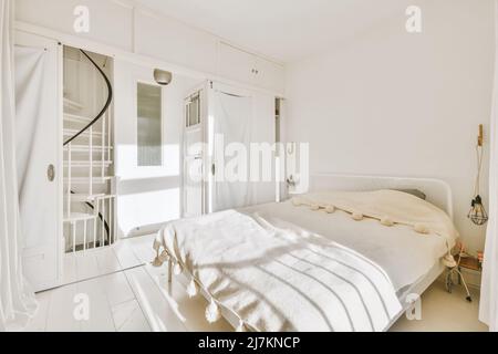 Comodo letto con coperta in camera da letto luminosa e lampada vicino scala in appartamento moderno Foto Stock