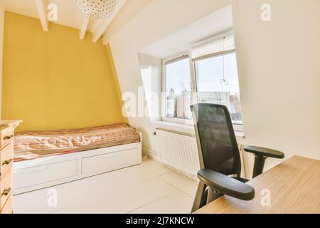 Comodo letto vicino alla scrivania della segretaria con sedia in camera da letto spaziosa e luminosa con finestre a casa Foto Stock