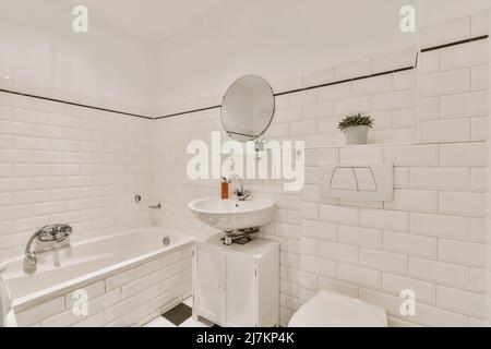 Interno di bagno bianco con pareti piastrellate arredate con vasca da bagno posta di fronte a ciotola wc sotto il soffitto inclinato Foto Stock