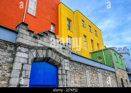 Recinzione in pietra con cancelli situati vicino all'esterno di casa residenziale multicolore contro il cielo blu sulla strada della città il giorno d'estate Foto Stock