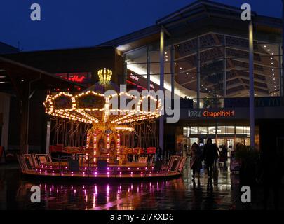 Giostra per bambini illuminata di notte, fuori dal centro commerciale Chapelfield nella città di Norwich, Norfolk, Inghilterra, Regno Unito Foto Stock