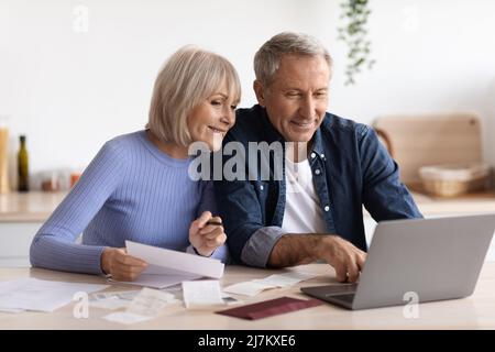 Coppia anziana felice che paga le fatture in linea, usando il calcolatore Foto Stock