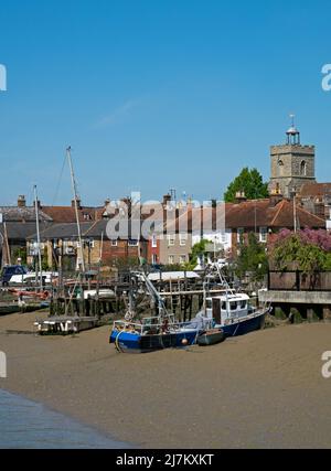 Barche ormeggiate sulla spiaggia di fronte all'estuario del fiume Colne, con gli antichi edifici della città di Wivenhoe, Essex, Inghilterra, Regno Unito Foto Stock