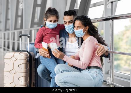 Famiglia araba di viaggiatori che indossano maschere mediche utilizzando lo smartphone in aeroporto Foto Stock