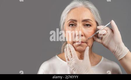 Bella donna anziana usando la medicina per iniezione per prevenire l'invecchiamento, ricevendo i colpi di bellezza di collagene o acido ialuronico Foto Stock