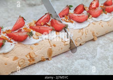 La pasticceria dello chef taglia con un grande coltello da cucina preparato e decorato con crema cremosa e fette di rotolo di meringa di fragole fresche Foto Stock