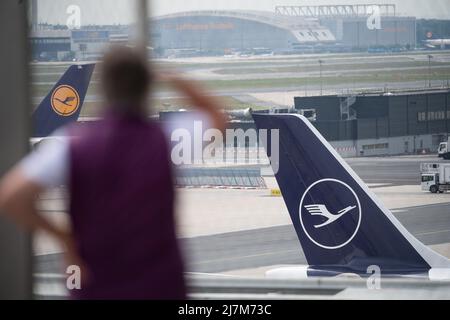 10 maggio 2022, Hessen, Francoforte sul meno: Una donna guarda in direzione di un velivolo con il logo Lufthansa sulla sua pinna di coda all'aeroporto di Francoforte. Nel frattempo, si svolge l'assemblea generale annuale della compagnia aerea Lufthansa. (A dpa 'Lufthansa CEO: Piena capacità possibilmente prima del 2025') Foto: Sebastian Gollnow/dpa Foto Stock