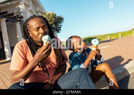 Padre e figlio afro-americani che si godono gelato sul lungomare nella soleggiata giornata estiva Foto Stock