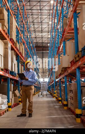 Giovane operaio africano americano con appunti che controlla scatole di cartone su scaffali in magazzino Foto Stock