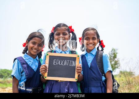 Gruppo di ragazzi adolescenti Village ragazza nella scuola uniforme tenendo ardesia con scritti di istruzione guardando la macchina fotografica - concetto di sviluppo, istruzione e. Foto Stock