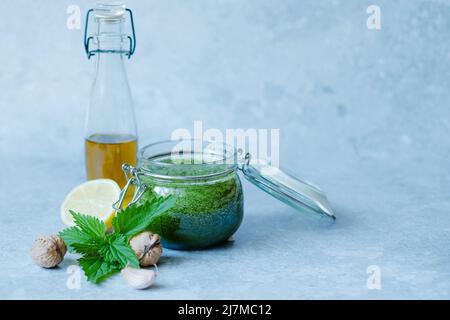 Pesto di ortica vegana con aglio, limone, olio d'oliva e noce. Vaso aperto di pesto di ortica fatto in casa su uno sfondo grigio. Foto Stock