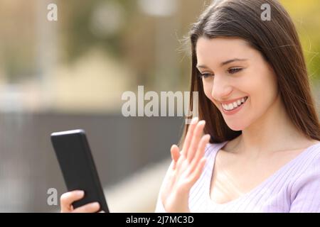 Felice donna saluto durante una videocall sul cellulare in strada Foto Stock