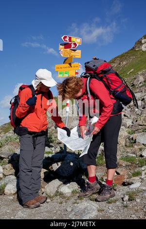 Svizzera, Alpi svizzere nel cantone di Graubünden. I turisti stanno controllando la loro mappa per essere sicuri circa il percorso. Anche un palo con segnali indica la strada Foto Stock