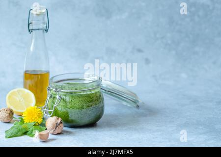 Aprire il vaso vegan dente di leone pesto con aglio, limone, olio d'oliva e noce su sfondo grigio. Foto Stock