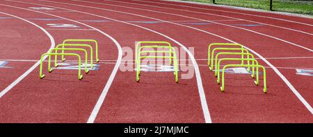 Tre file di mini ostacoli gialli allestiti in corsie su una pista per allenarsi in modo agile durante la pratica su pista e sul campo. Foto Stock