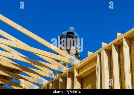 Vista aerea di un costruttore sul tetto non finito con travi in legno chiodate in casa a telaio in costruzione Foto Stock